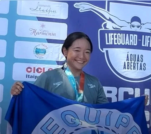 Ana com a medalha e a bandeira da Navegantes, no cartão de resultados da equipe.
